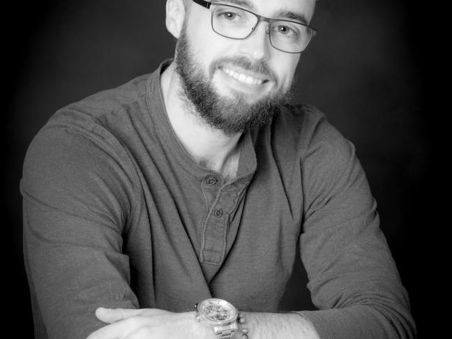 Photographie de l'auteur en noir et blanc. Il porte la barbe et des lunettes, à les bras croisés et regarde l'objectif de trois-quart.