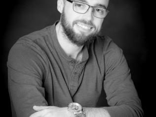 Photographie de l'auteur en noir et blanc. Il porte la barbe et des lunettes, à les bras croisés et regarde l'objectif de trois-quart.